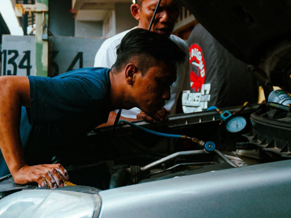 Medium shot of two mechanics looking closely into an open vehicle hood during engine diagnostics.