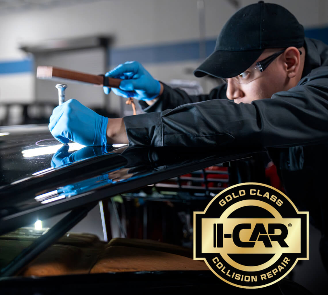 Medium close-up shot of an I-CAR collision technician repairing a black vehicle's bodywork.