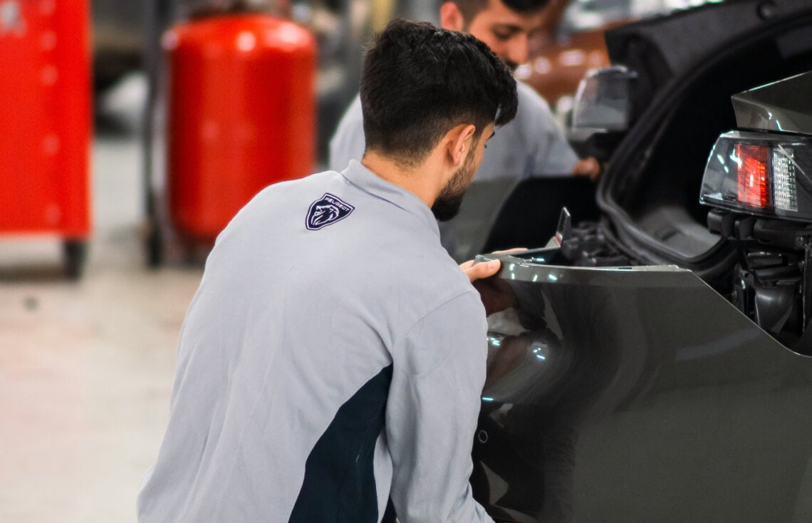 Medium close-up shot of an auto body technician aligning a vehicle's rear bumper panel.