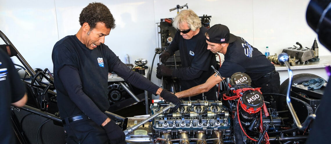 Medium shot of a pit crew team using specialized tools to tune a car engine in a garage