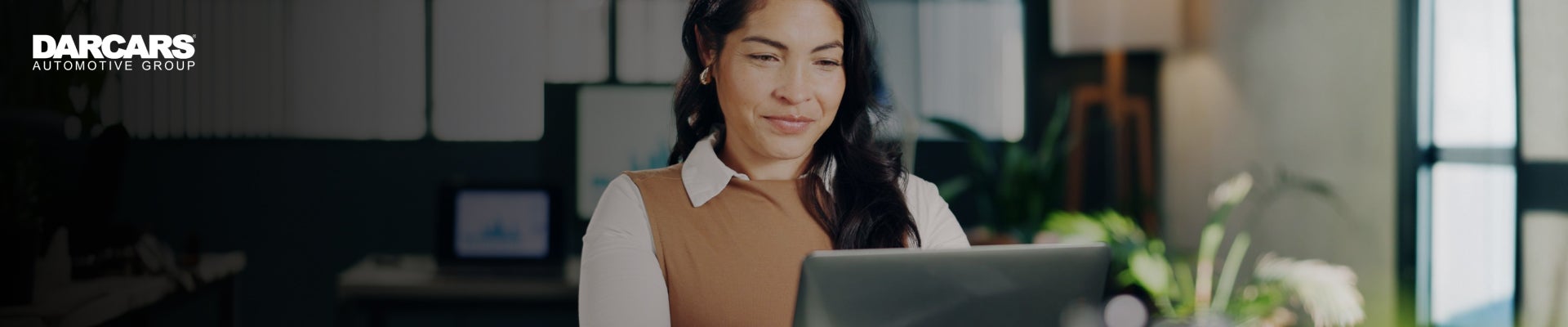 A woman sitting at a desk typing on her computer with the DARCARS Automotive Group logo shown.